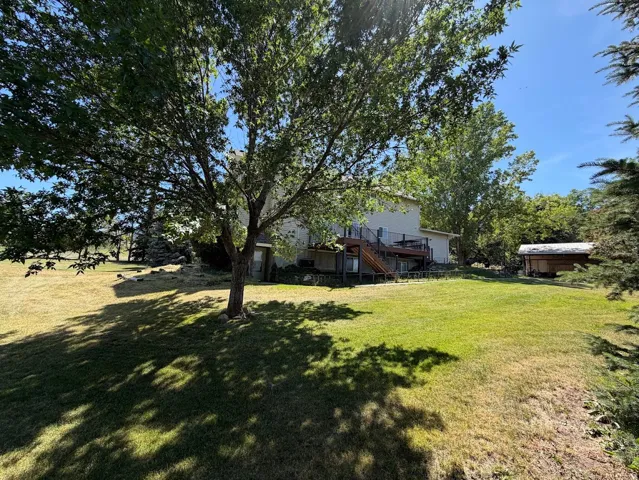 Spacious backyard featuring a large green lawn, mature trees, a multi-level deck with wood stairs and white railings, and a detached wooden shed