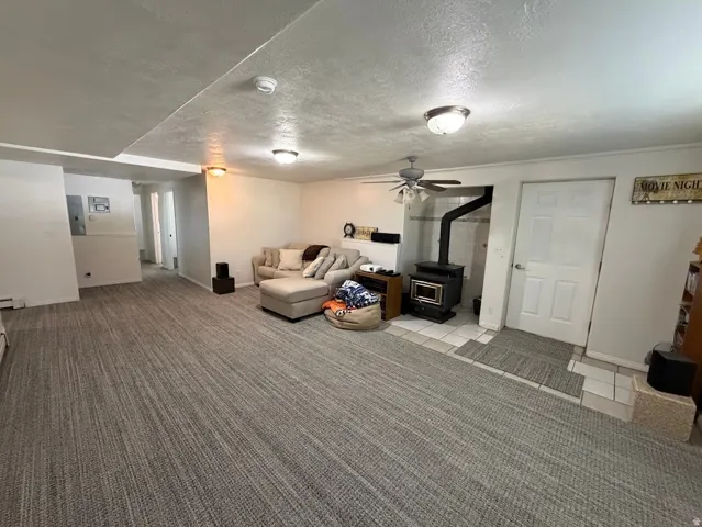 Spacious entertainment area featuring textured carpet flooring, a corner-situated wood-burning stove with a tiled hearth, and recessed lighting