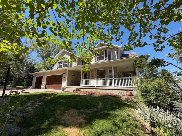 Two-story property featuring a wrap-around porch with white railings, a multi-car garage with wood-finish doors, and dormer windows on the upper level