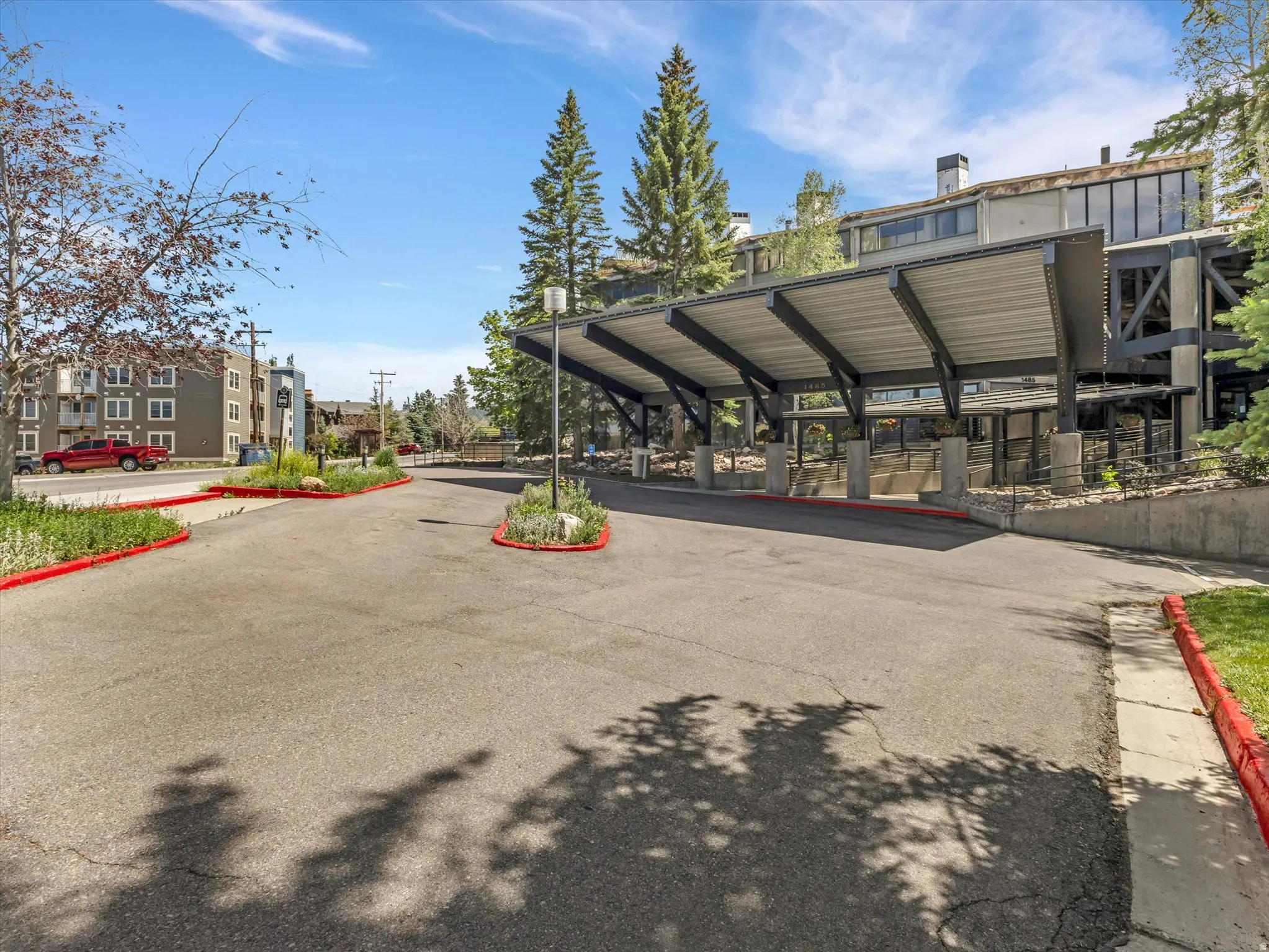 Covered entryway with a substantial porte-cochere structure, featuring exposed beams and a wide asphalt driveway