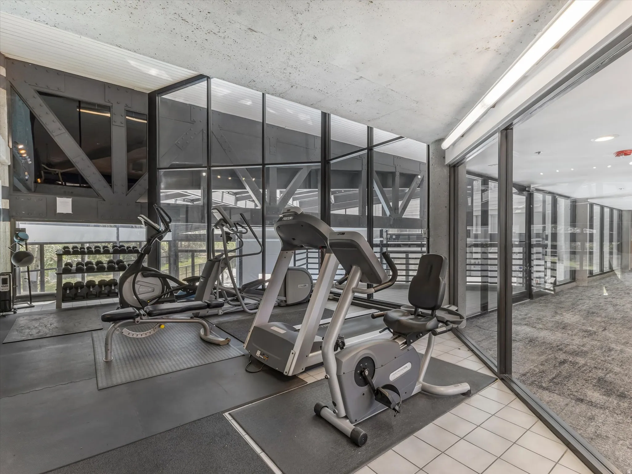 Fitness center featuring a concrete ceiling, full-height windows, a selection of exercise equipment, and dedicated rubber flooring