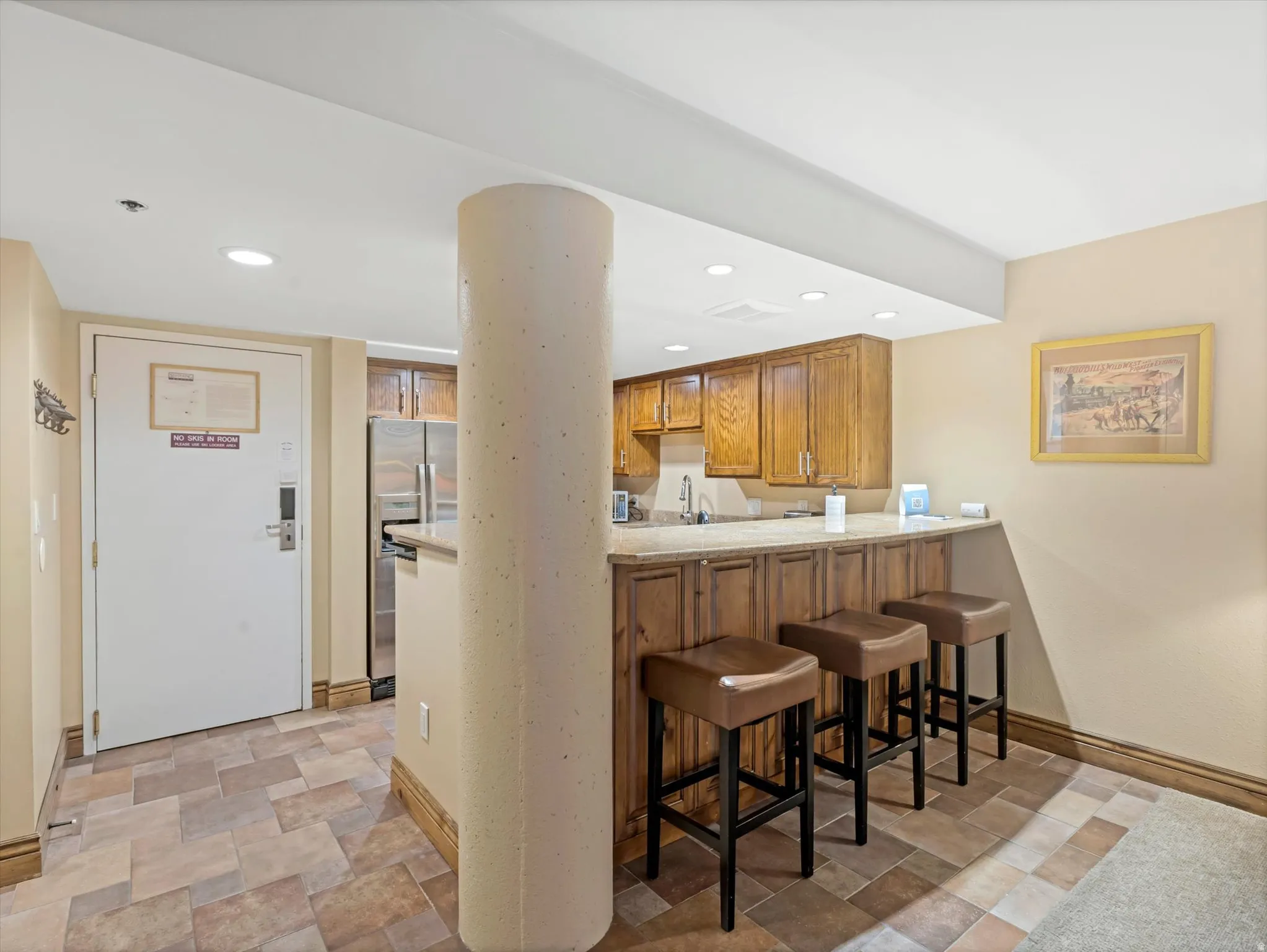 Kitchenette featuring wood cabinetry, stainless steel refrigerator, and built-in bar seating with three stools