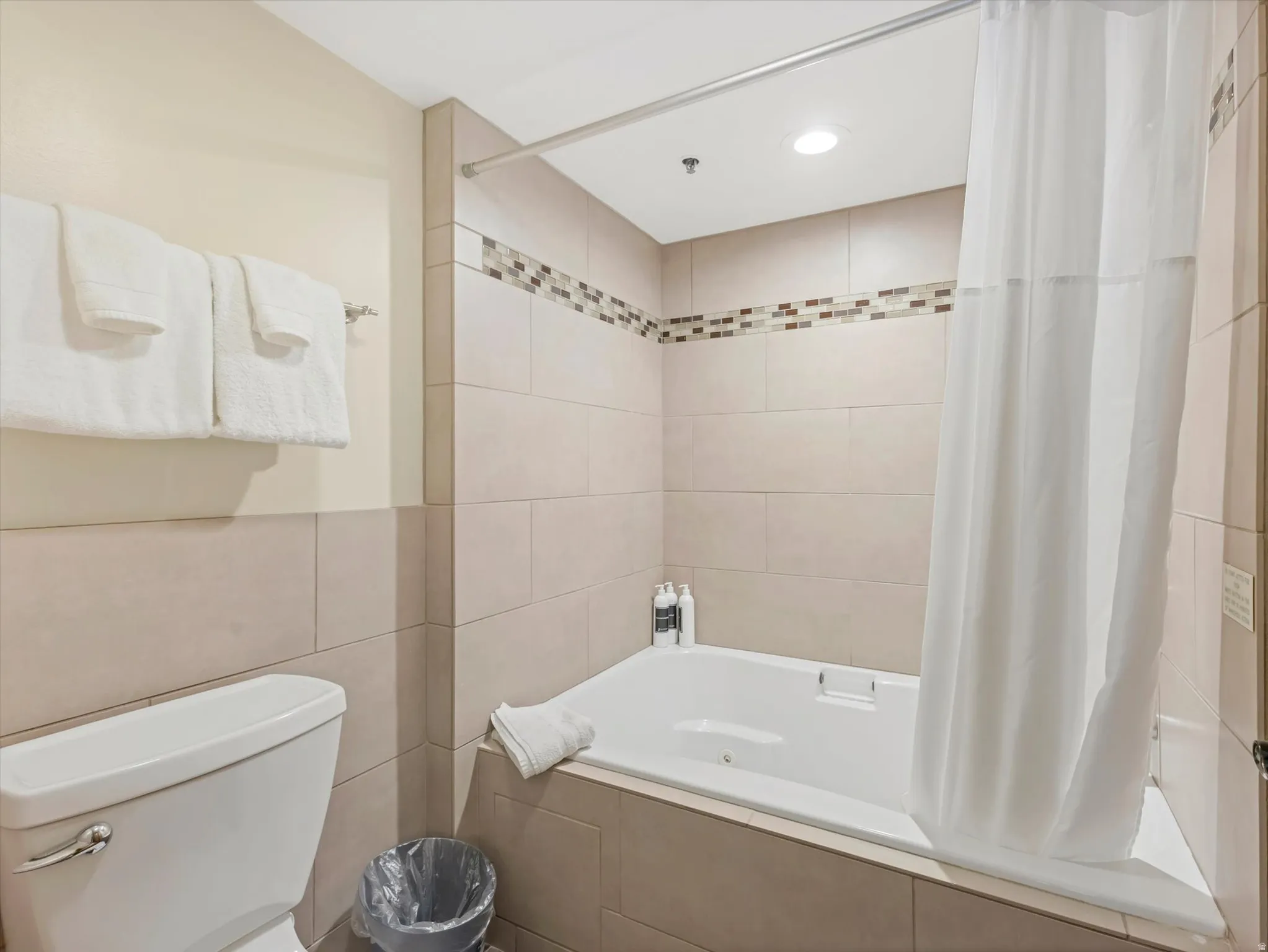 Recessed bath with a white shower curtain, light-colored tile surround, and decorative mosaic accent band