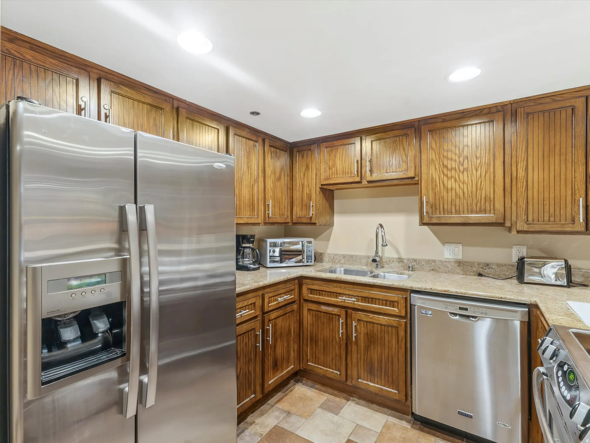 Kitchen featuring wood cabinetry, stainless steel appliances, a double basin sink with a gooseneck faucet, light-toned countertops, and mosaic-style floor tiles