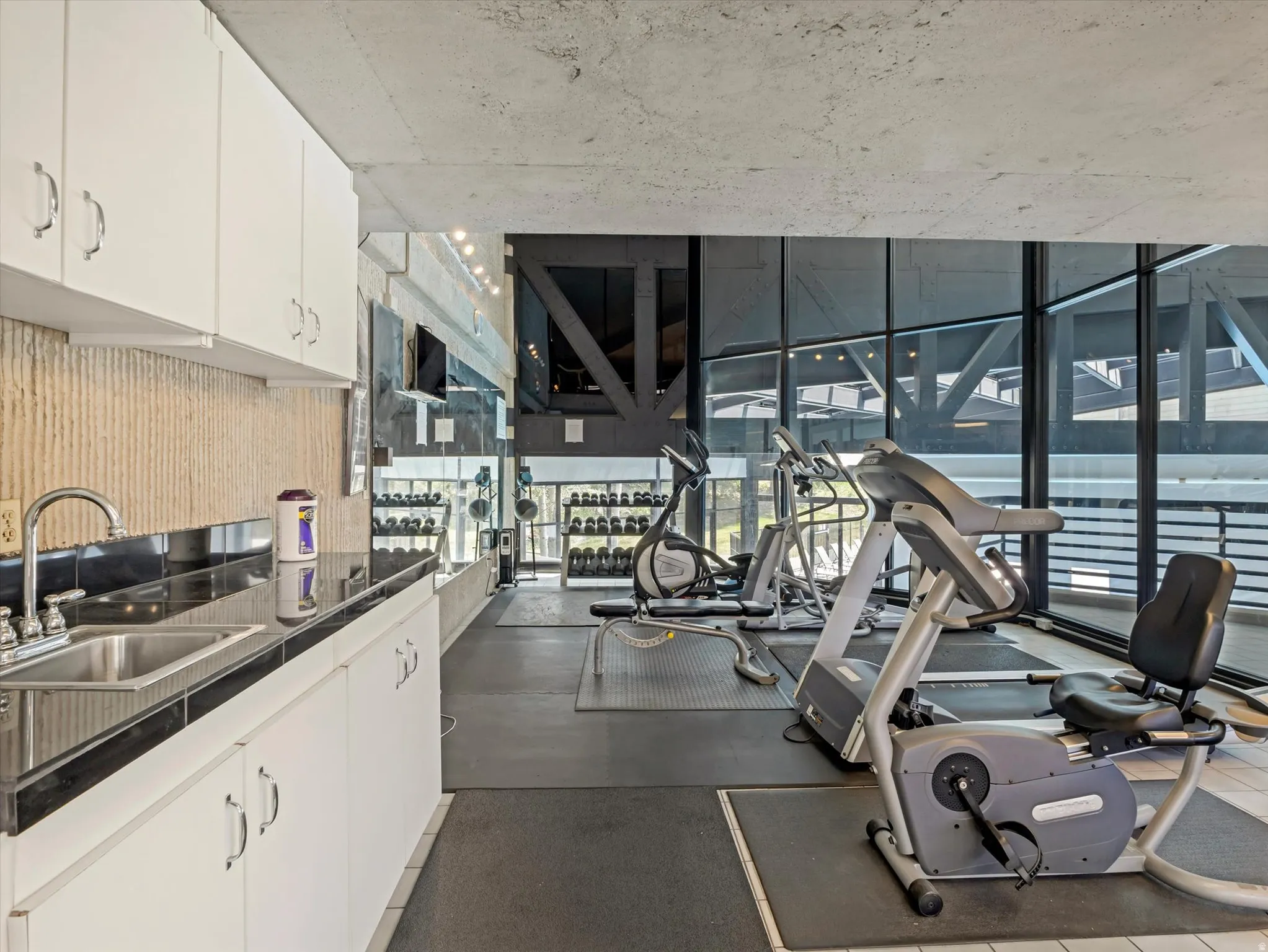 Fitness area featuring large windows, exposed concrete ceiling, and rubber flooring