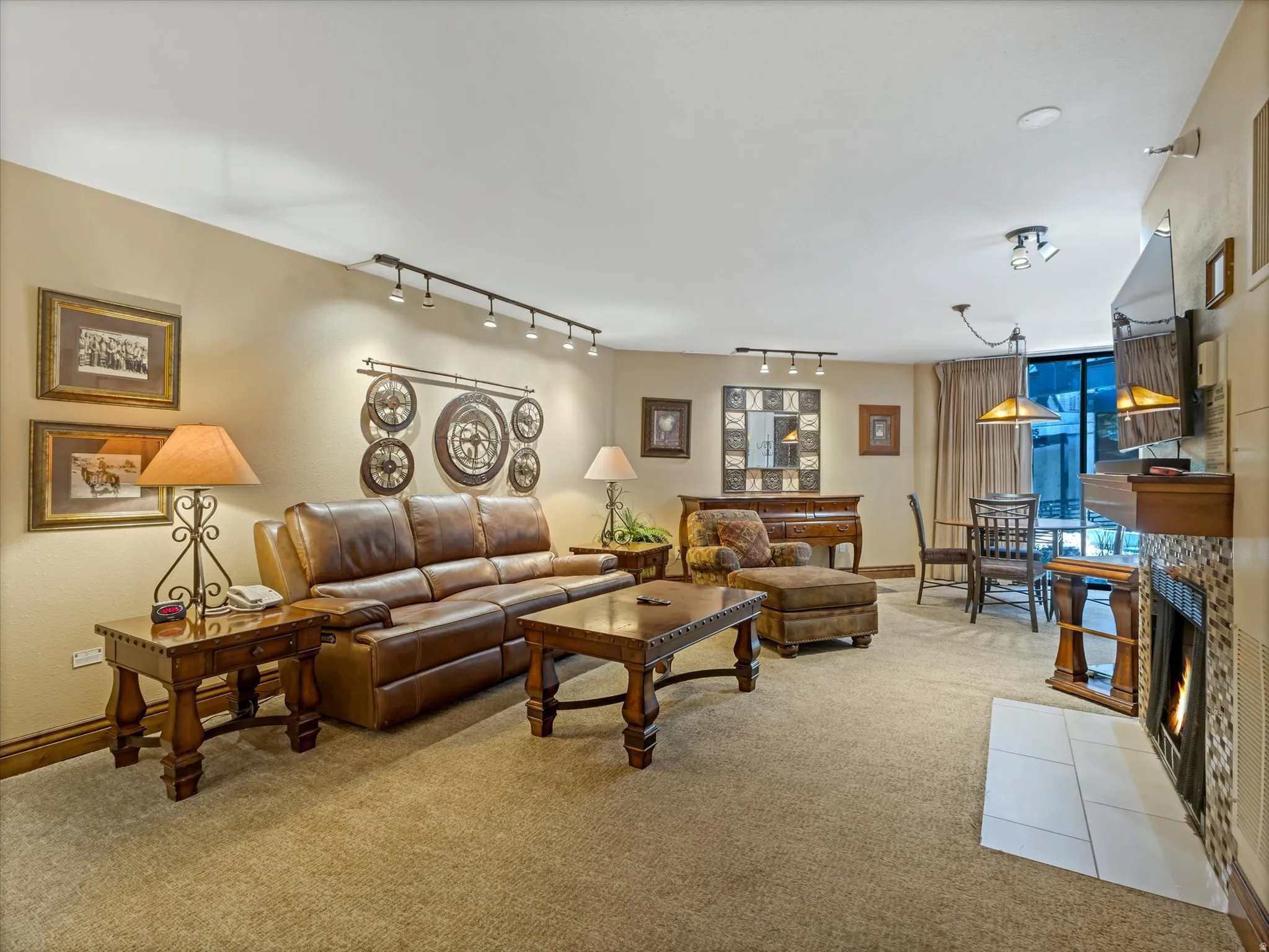 Carpeted living area featuring track lighting, built-in fireplace with tile surround, and a dining area with pendant lighting