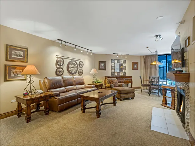 Carpeted living area featuring track lighting, built-in fireplace with tile surround, and a dining area with pendant lighting