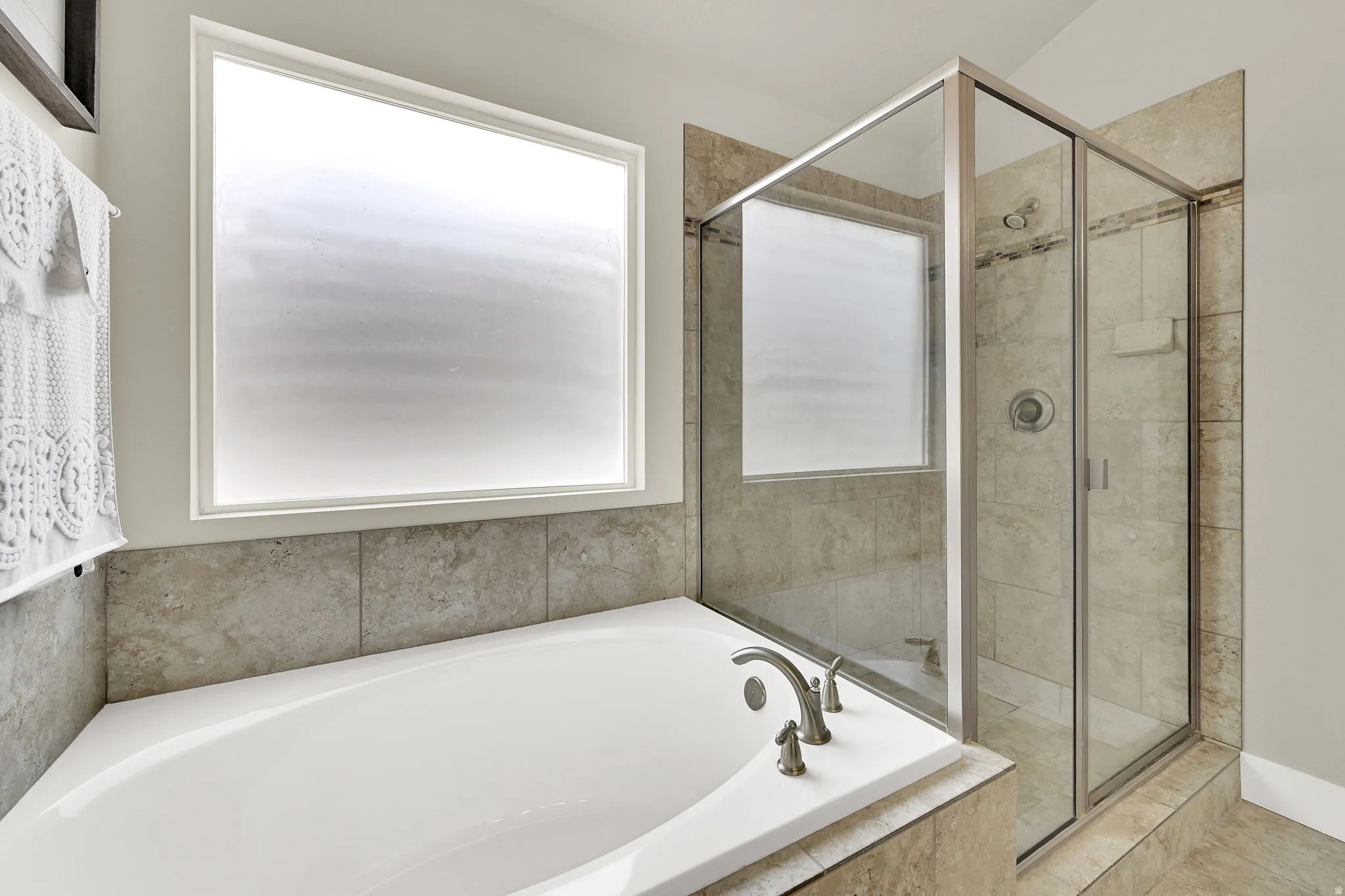 Soaking tub with brushed nickel fixtures, surrounded by large format tile, alongside a glass-enclosed shower with tile surround