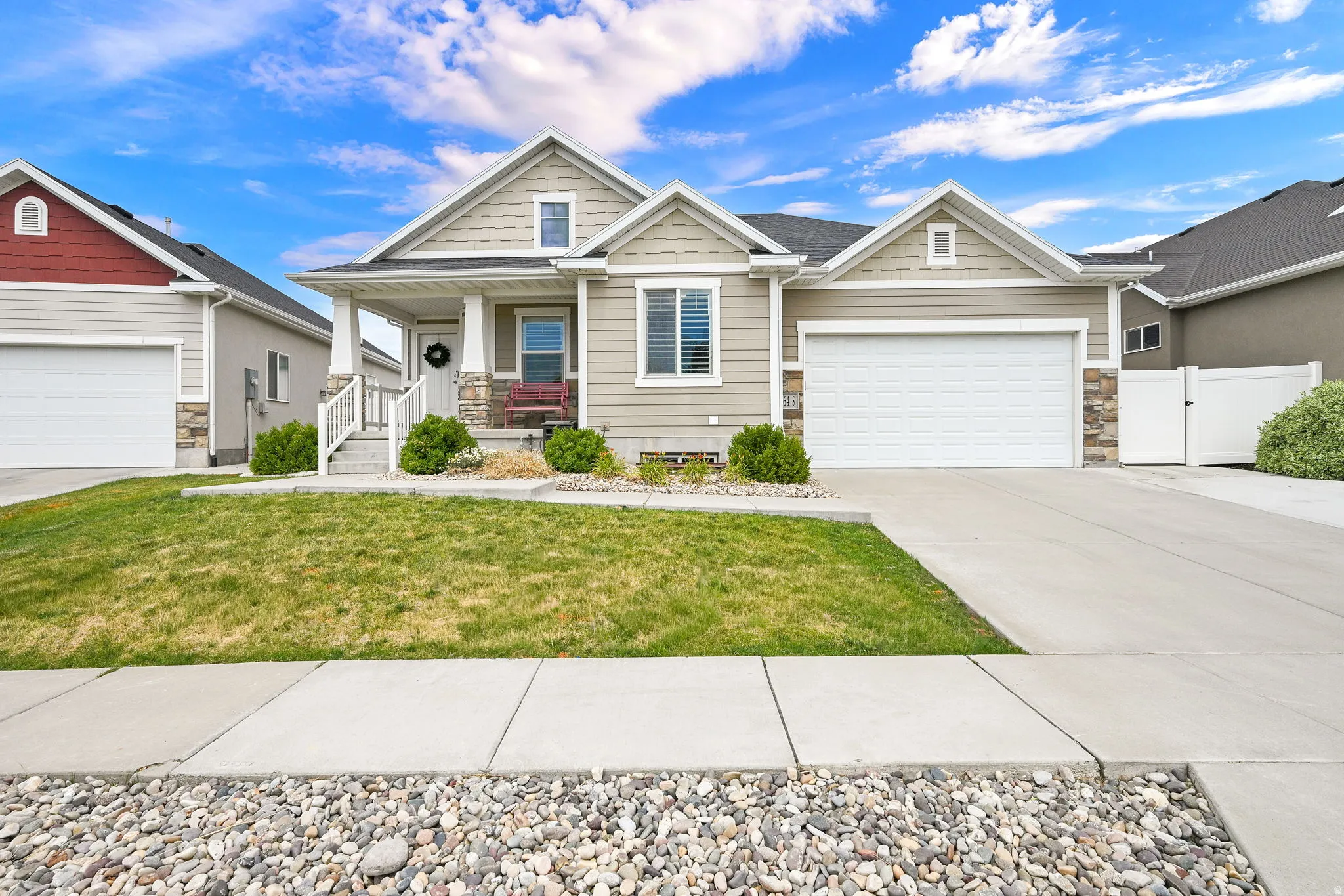 Ranch-style residence featuring light-colored siding, a covered front porch with white columns, stone accents, and two distinct garage doors