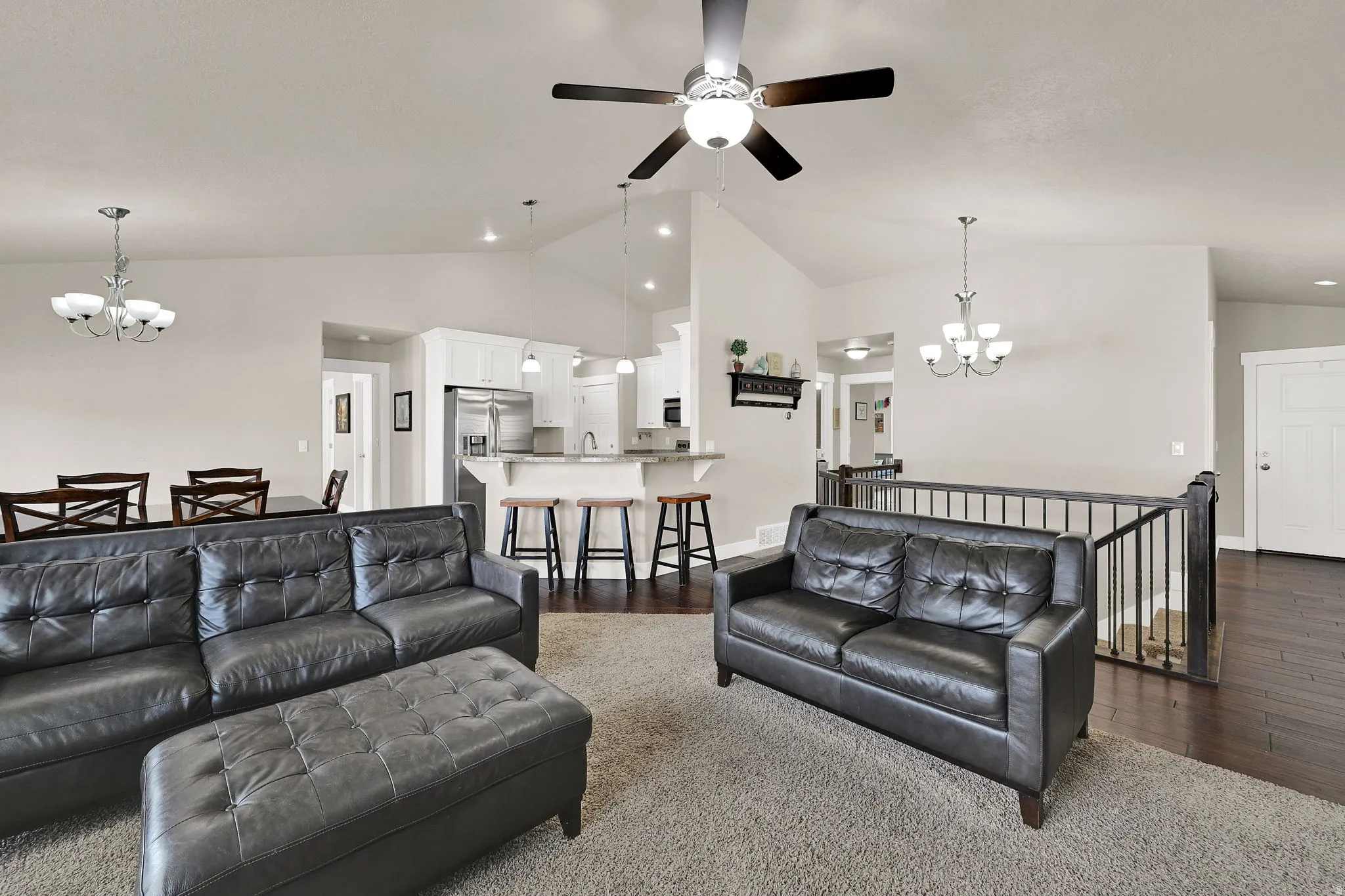 Vaulted ceilings featuring a ceiling fan, a kitchen with white cabinetry and stainless steel appliances, a breakfast bar, dark wood-finish flooring, and a stairway with black metal spindles