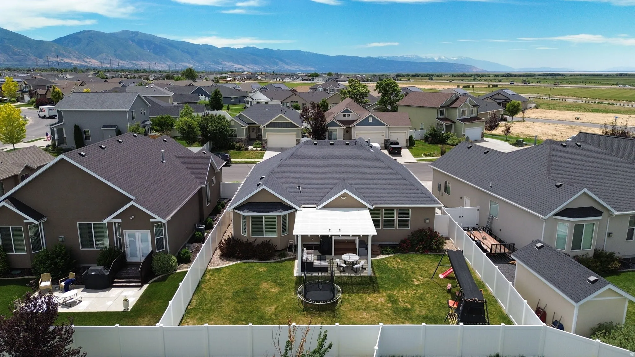 Expansive backyard featuring a manicured lawn, white privacy fencing, and a covered patio area