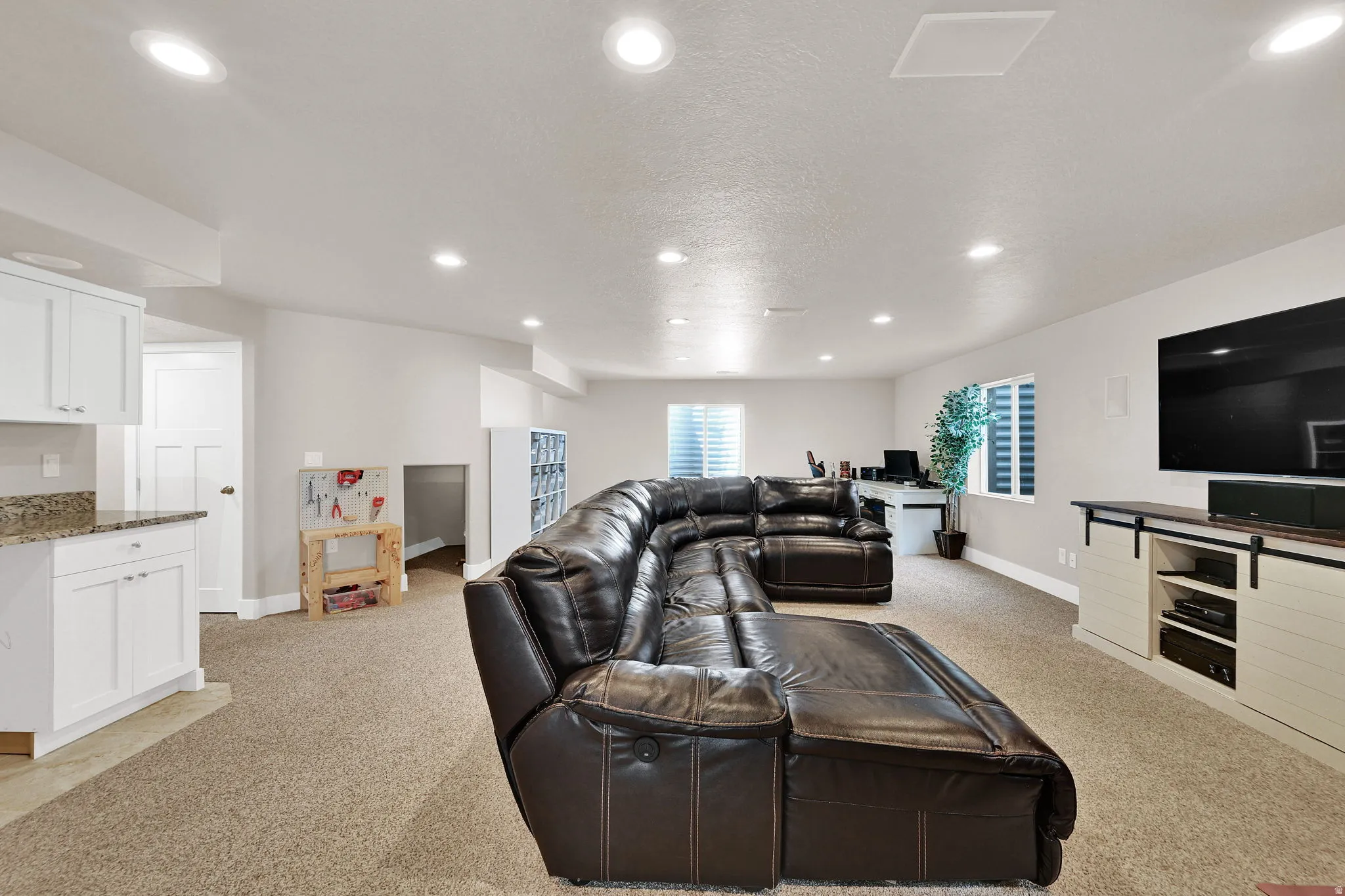 Spacious recreational room featuring recessed lighting, light beige carpet, and a built-in entertainment console with sliding barn door style cabinet fronts