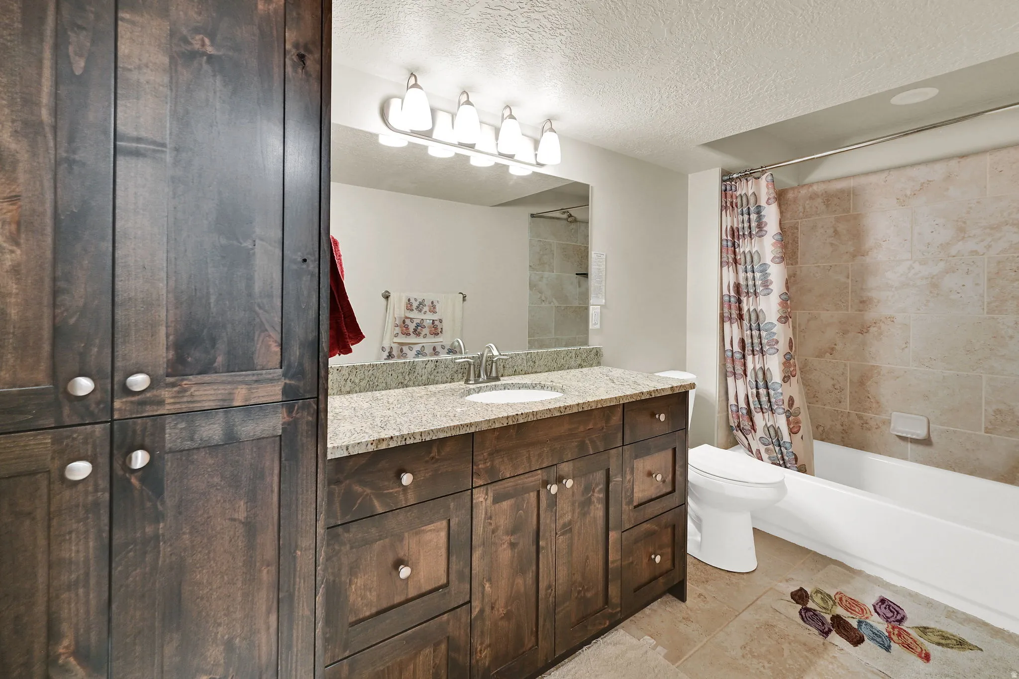 Bathroom featuring a single-sink vanity with a granite countertop, wood-finish cabinetry, and an integrated tub-shower combination with tile surround