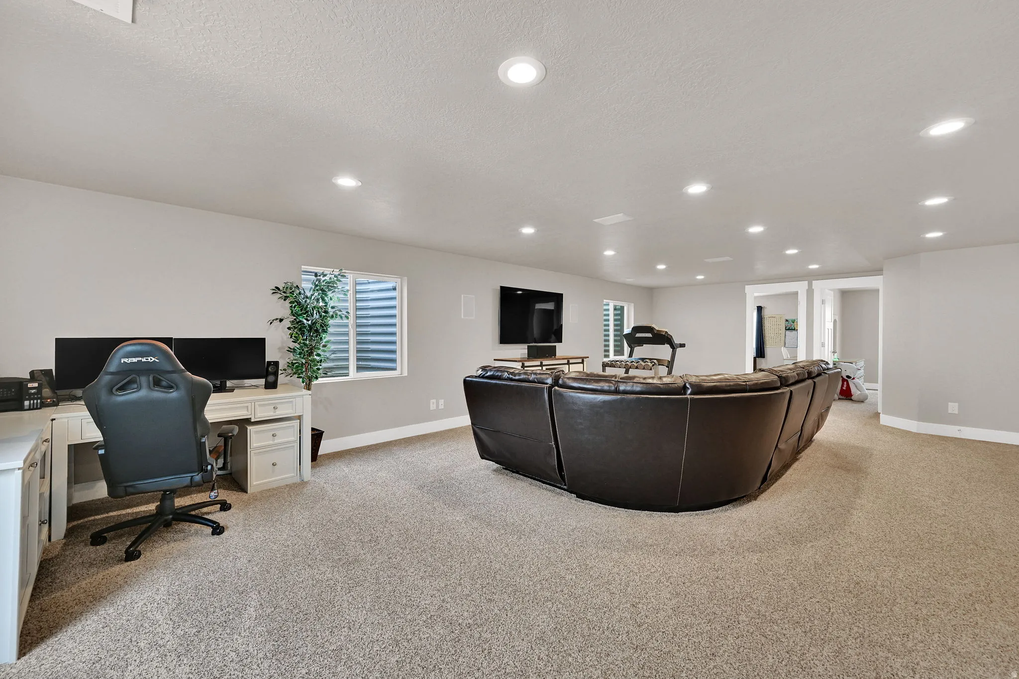 Spacious lower-level area featuring recessed lighting, light-toned carpeting, a window with horizontal blinds, and a built-in desk with cabinet storage