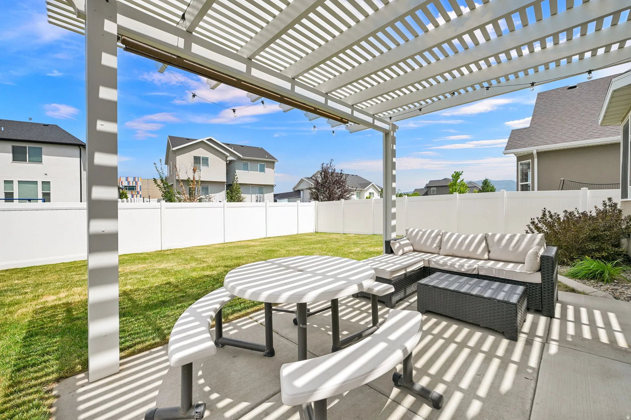 Expansive concrete patio area with a white slatted pergola