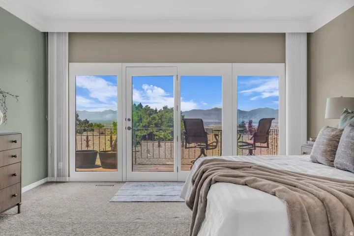 Bedroom featuring a private balcony with mountain scenery, white French doors, crown molding, light gray carpet, and neutral wall tones