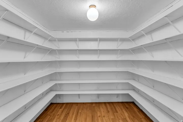 Spacious storage room featuring extensive built-in shelving, durable wood-finish flooring, and overhead illumination