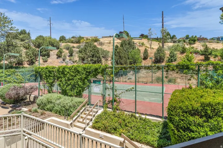 Tennis court with a red and green playing surface, bordered by chain-link fencing and mature landscaping