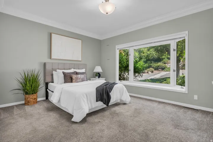 Spacious room featuring a multi-pane bay window, crown molding, light gray wall paint, and gray carpeting