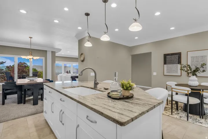 Spacious kitchen island featuring a stone countertop, an undermount sink with a gooseneck faucet, and white base cabinetry with silver hardware