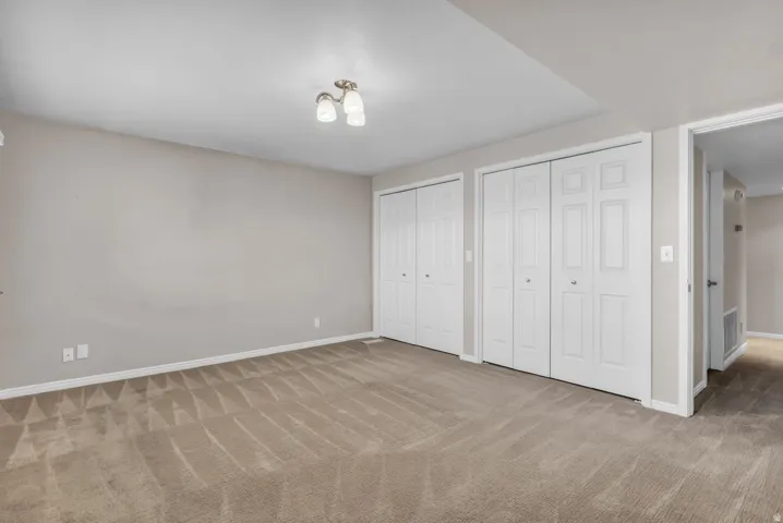 Carpeted room featuring a ceiling-mounted light fixture, two sets of bi-fold closet doors, and neutral wall tones