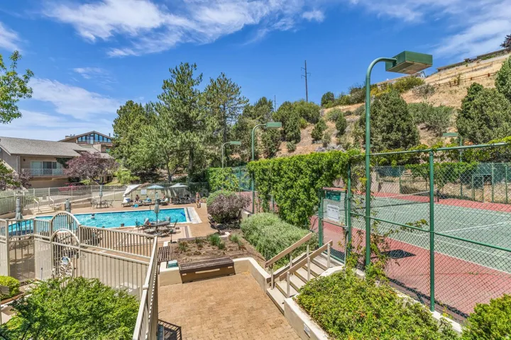 Community amenities featuring a tennis court with chain-link fencing, a swimming pool, and a surrounding patio area with lounge seating