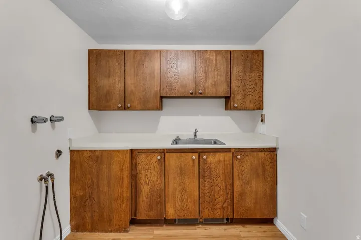 Dedicated utility area featuring wood-finish cabinetry, a utility sink with a chrome faucet, light-toned countertops, and wood-finish flooring
