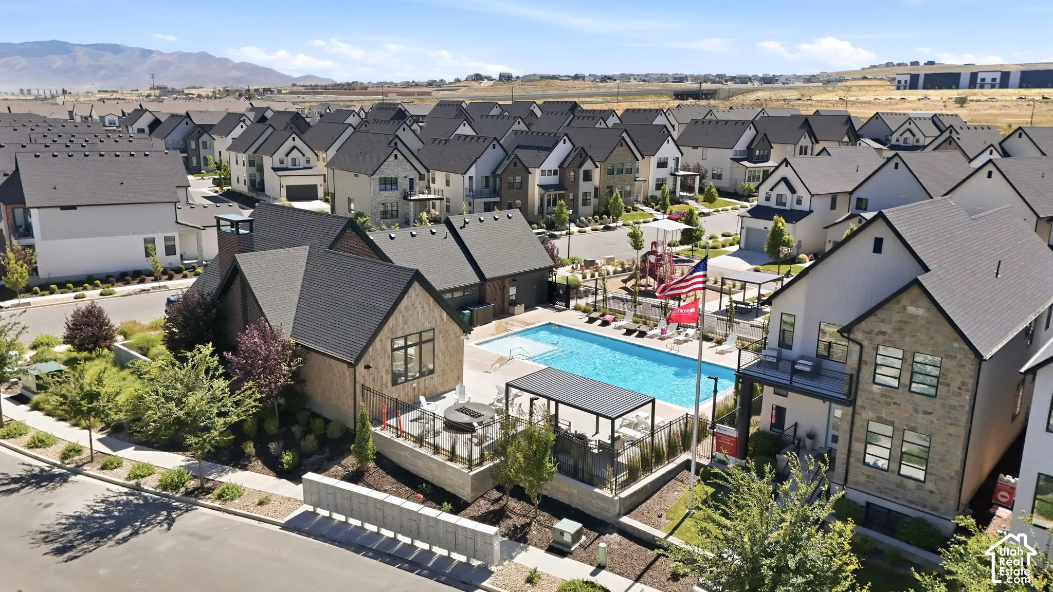 Community pool and clubhouse amenity featuring a rectangular swimming pool, multiple shaded seating areas, a children's play structure, and surrounding residential properties