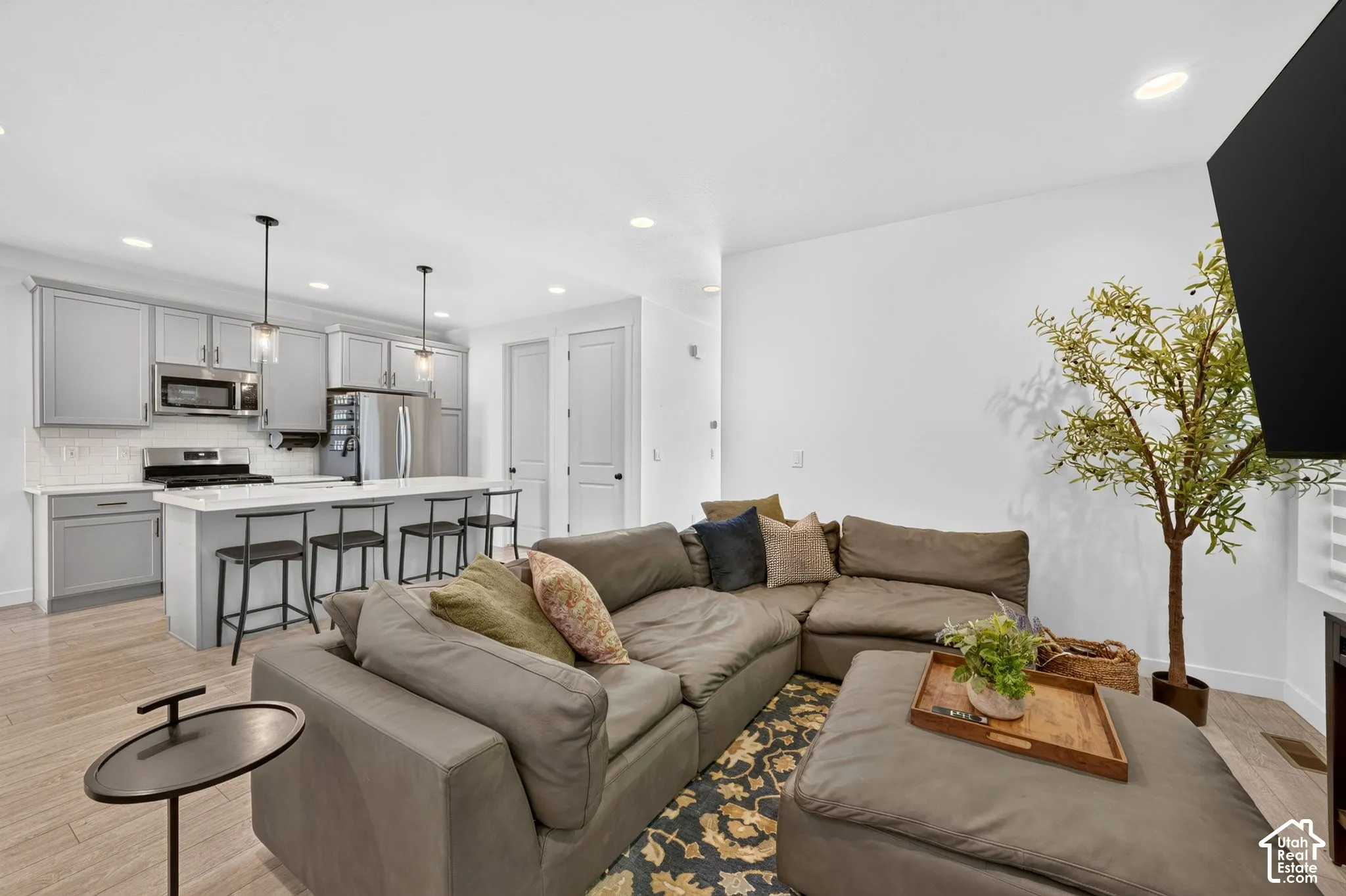 Open-concept living space featuring wood-finish flooring, a kitchen island with seating, pendant lighting, stainless steel appliances, and light gray cabinetry