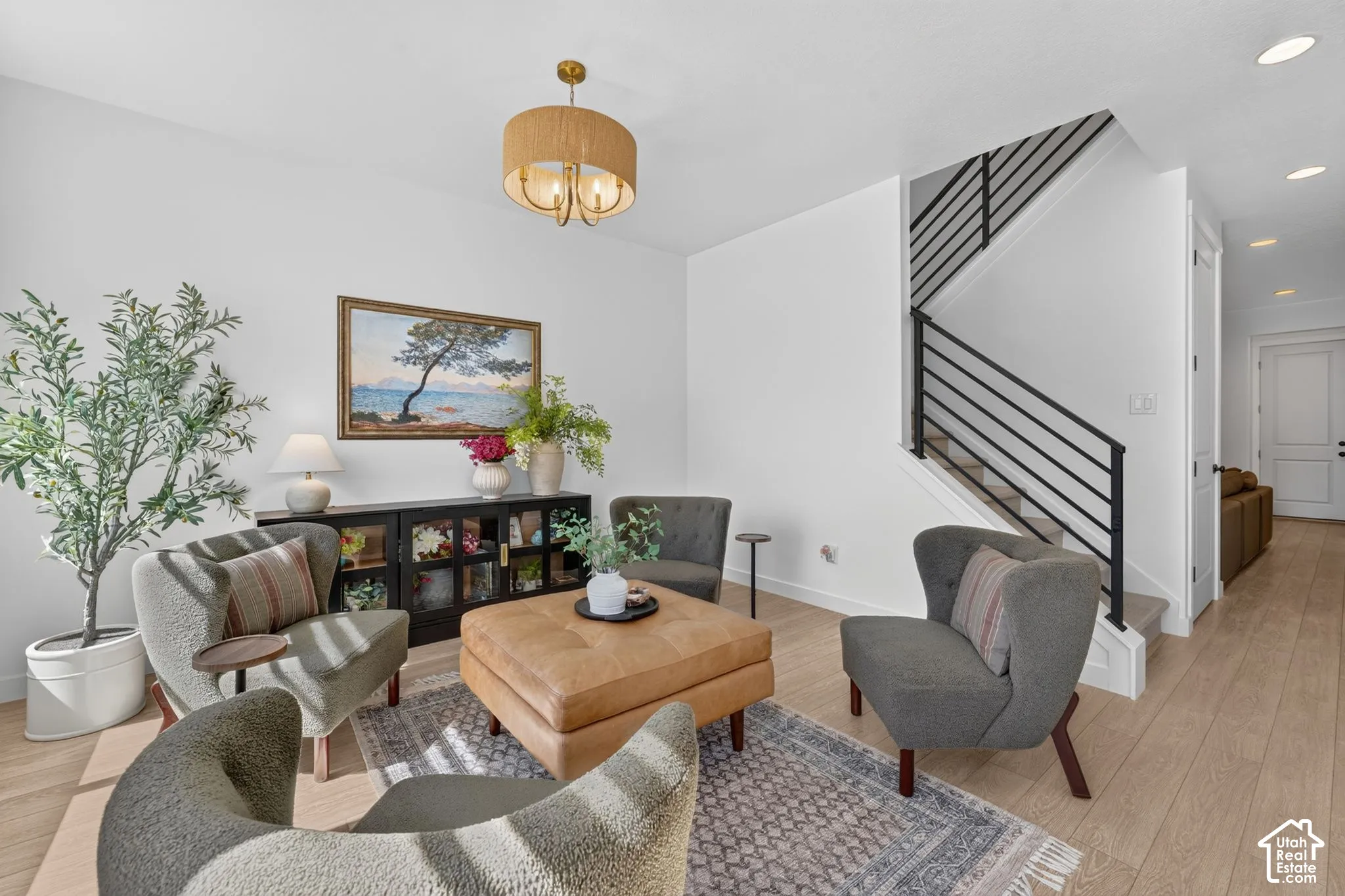 Open-concept living space featuring wood-finish flooring, a contemporary black metal stair railing, and a drum-style ceiling light fixture