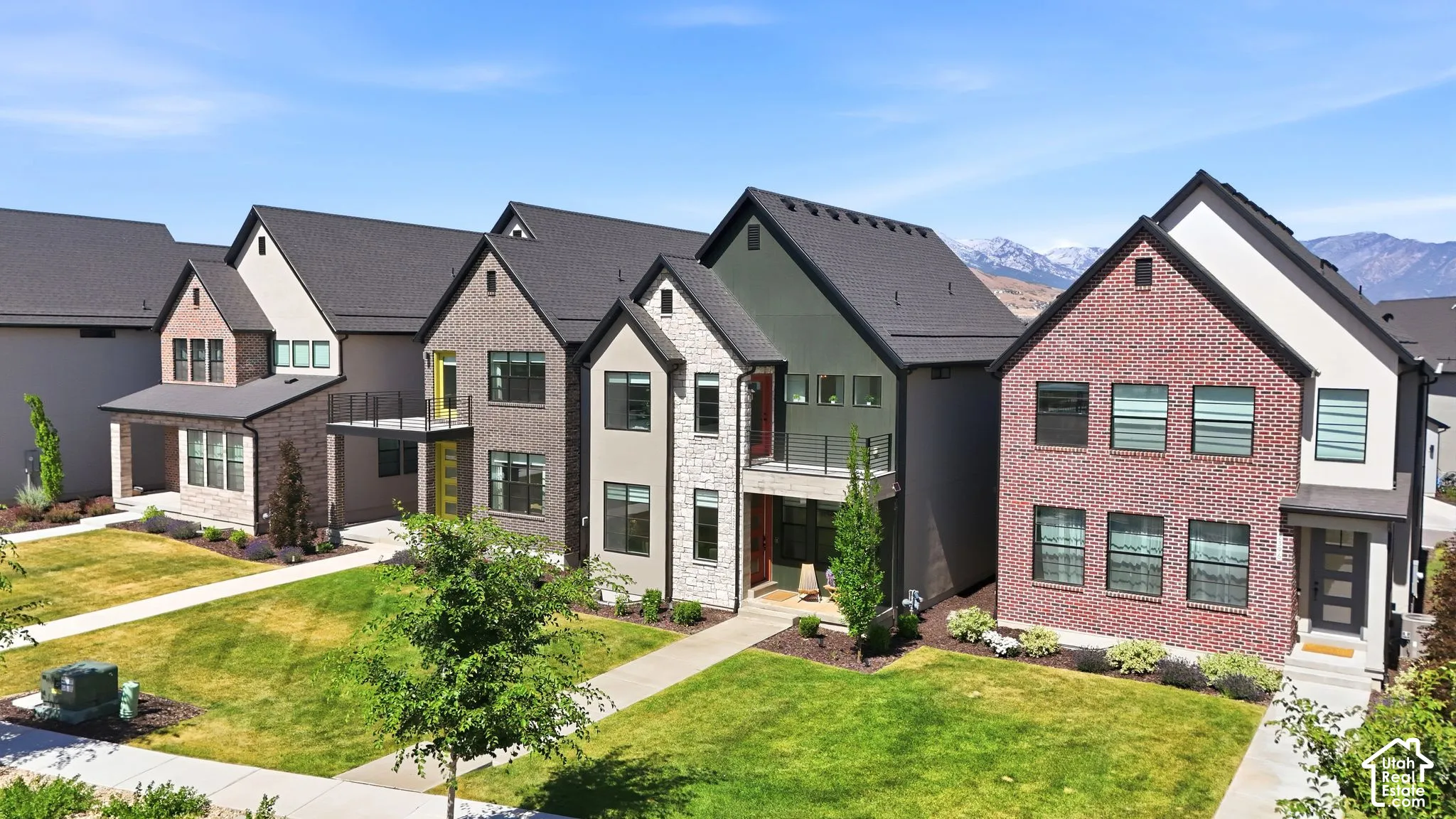 Modern residential architecture featuring a variety of exterior finishes including brick and stone, dark-framed windows, and a paved walkway