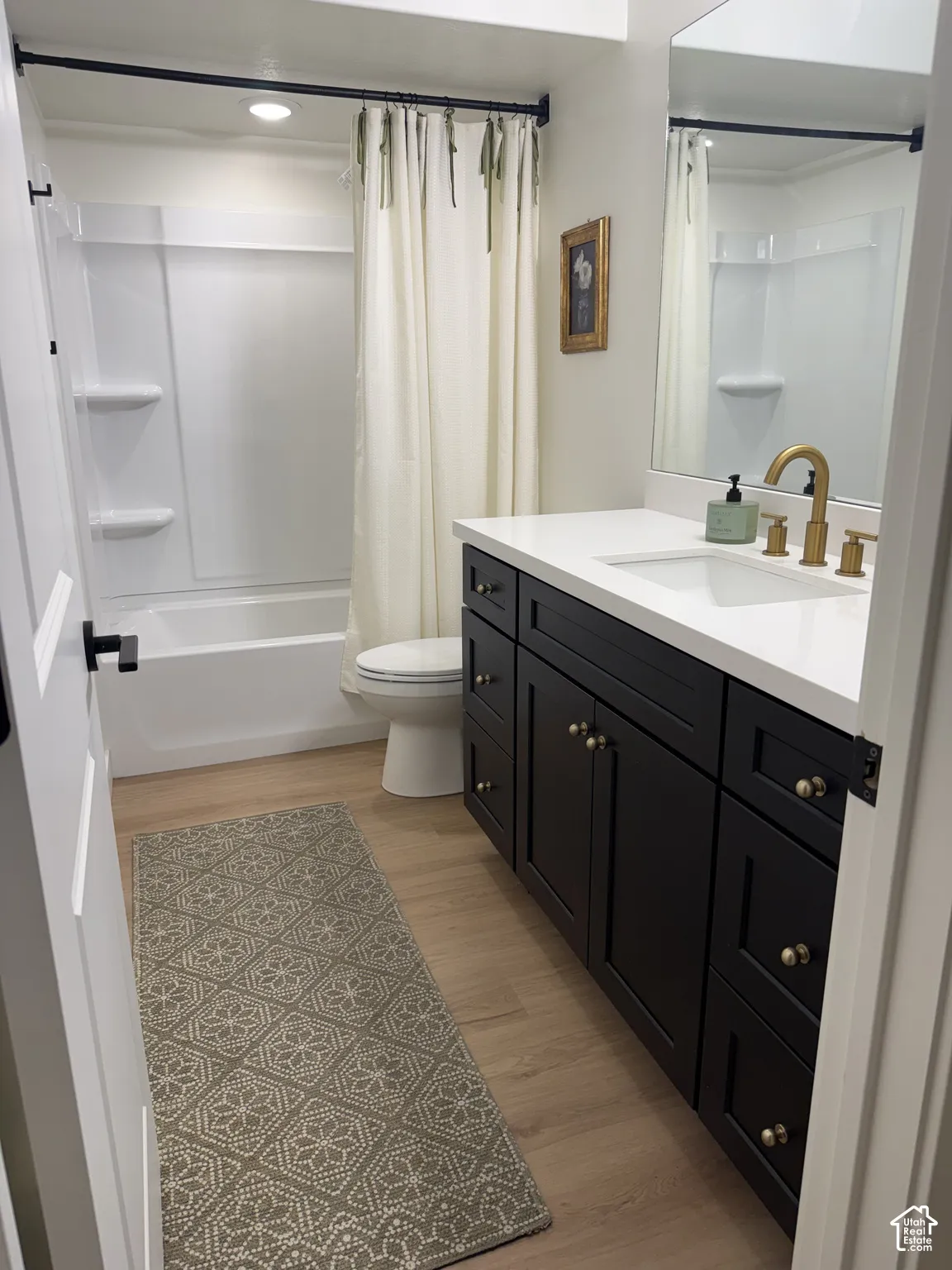 Bathroom featuring a full vanity with a white countertop, an undermount sink, and black cabinetry with brass-tone hardware