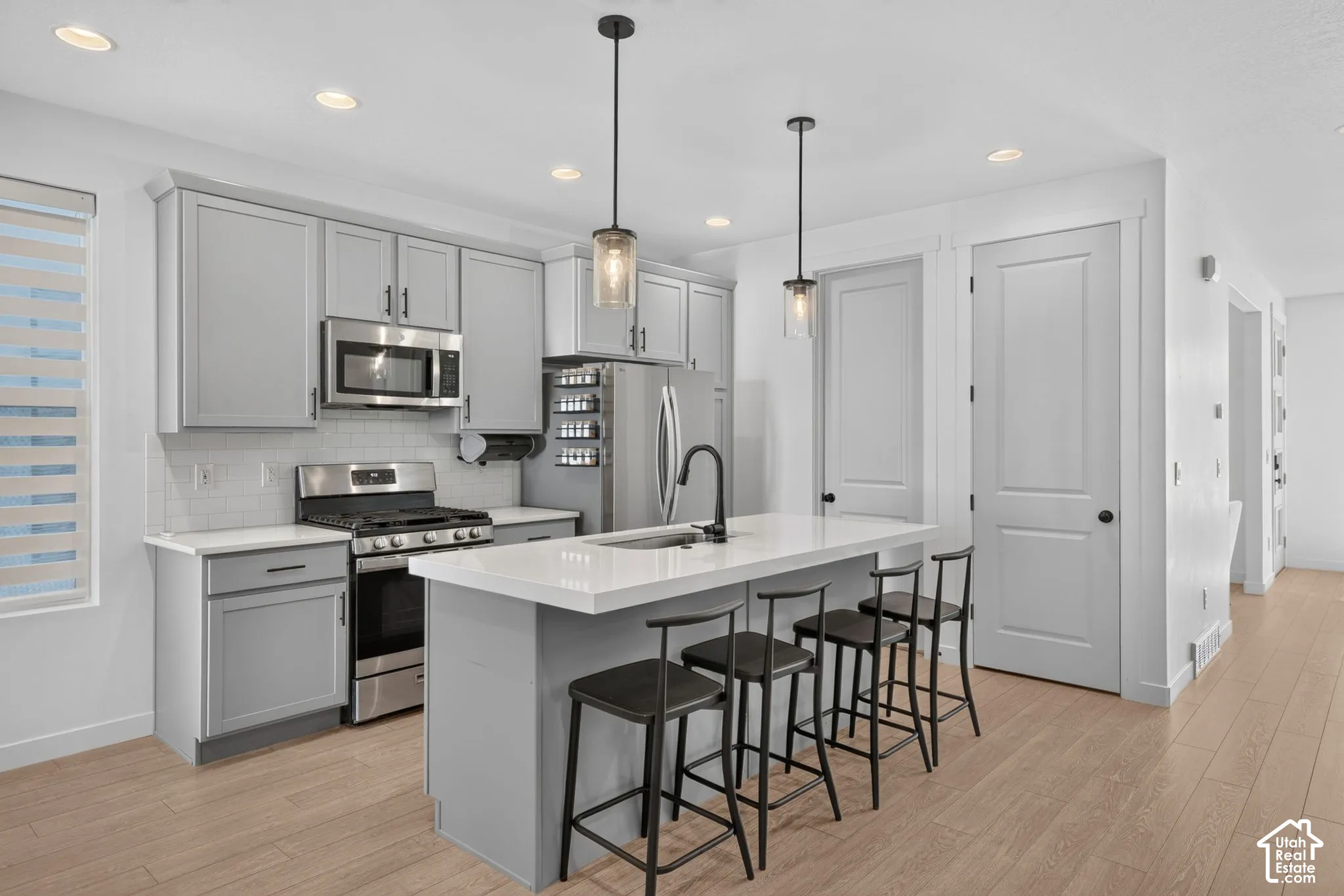 Modern kitchen with a central island, light wood-finish flooring, stainless steel appliances, light gray cabinetry, and recessed lighting