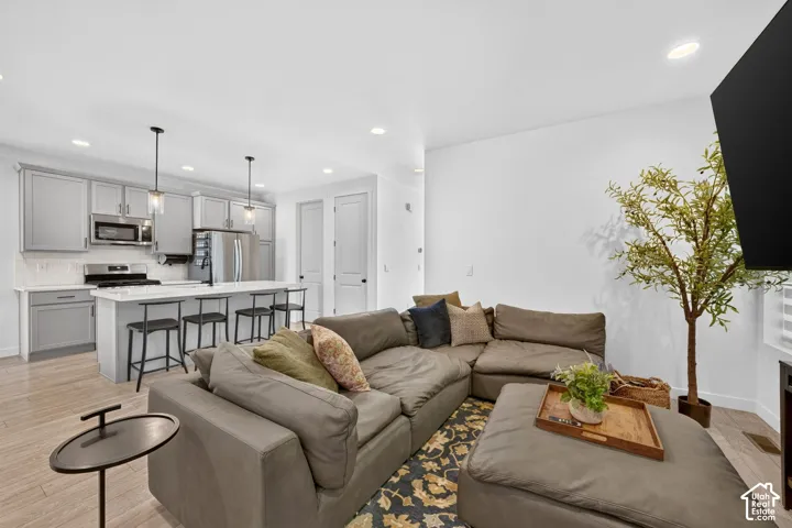 Open-concept living space featuring wood-finish flooring, a kitchen island with seating, pendant lighting, stainless steel appliances, and light gray cabinetry