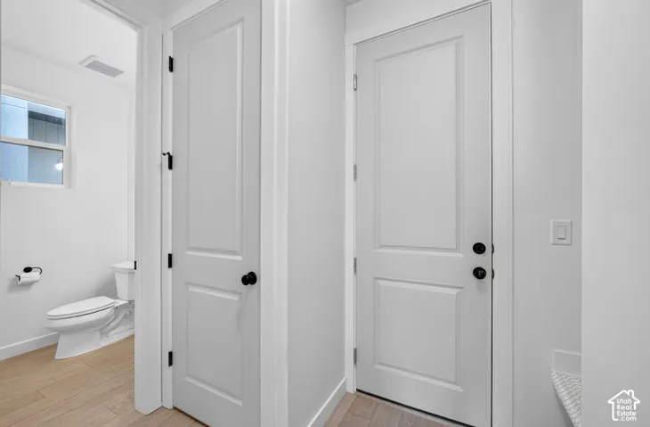 Hallway featuring two-panel interior doors with matte black hardware, light wood-finish flooring, and crisp white walls