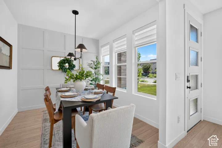 Dining area featuring light wood-finish flooring, a decorative panel accent wall, and multiple windows with blinds