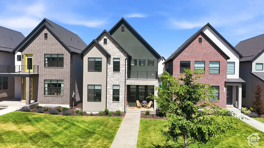 Contemporary multi-story residence featuring a mixed-material facade with stone accents, dark-framed windows, a covered entrance, and a balcony