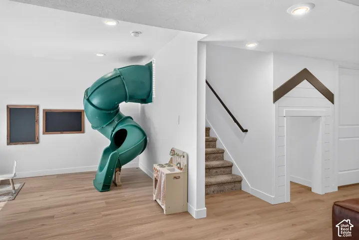 Recreation area featuring a built-in green slide, recessed lighting, wood-finish flooring, a carpeted staircase with a dark handrail, and a charming alcove with shiplap detailing