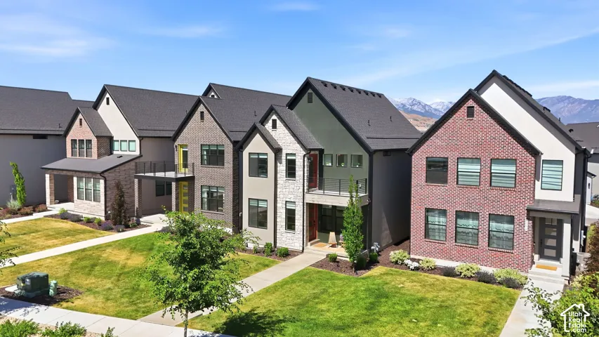 Modern residential architecture featuring a variety of exterior finishes including brick and stone, dark-framed windows, and a paved walkway