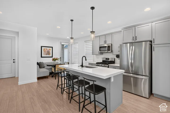 Open-concept kitchen featuring an island with counter seating, stainless steel appliances, light gray cabinetry, wood-finish flooring, and recessed lighting