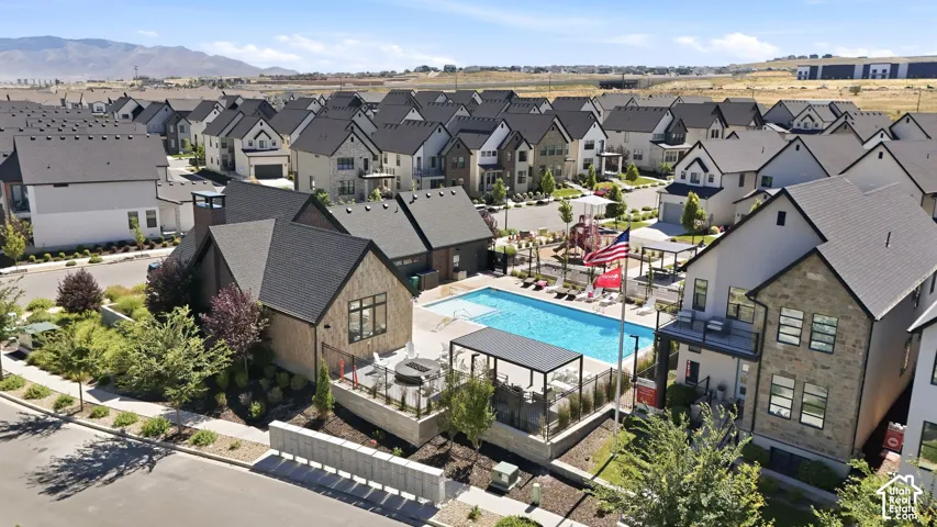 Community pool and clubhouse amenity featuring a rectangular swimming pool, multiple shaded seating areas, a children's play structure, and surrounding residential properties