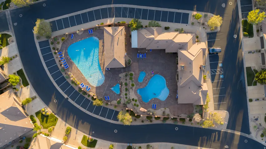 Community recreation area featuring multiple swimming pools, extensive patio space, surrounding landscaping, and dedicated parking