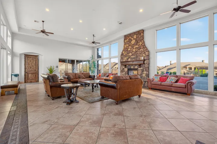 Spacious common area featuring a stone fireplace, large format tile flooring, high ceilings with recessed lighting, and multiple ceiling fans