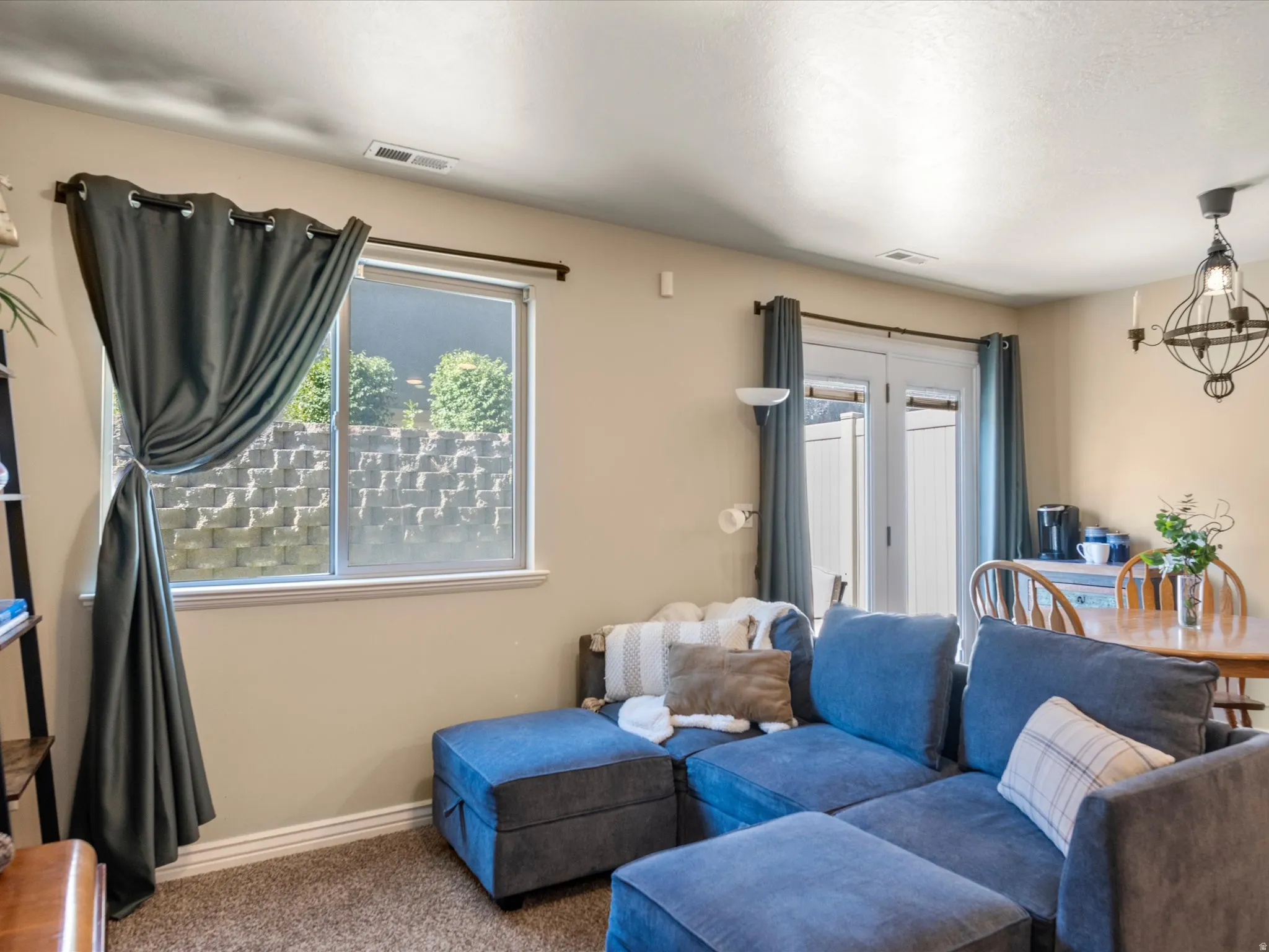 Living area featuring carpet flooring, a window with a stone block retaining wall visible outside, and a double patio door leading to an exterior space