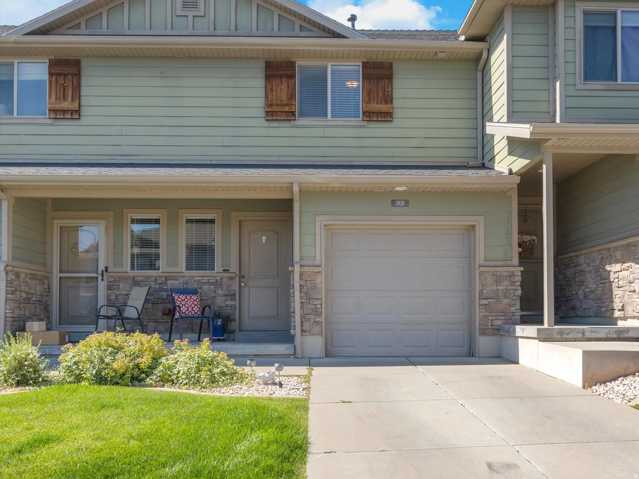Townhome exterior featuring light green siding, stone accents, and wood-finish window shutters