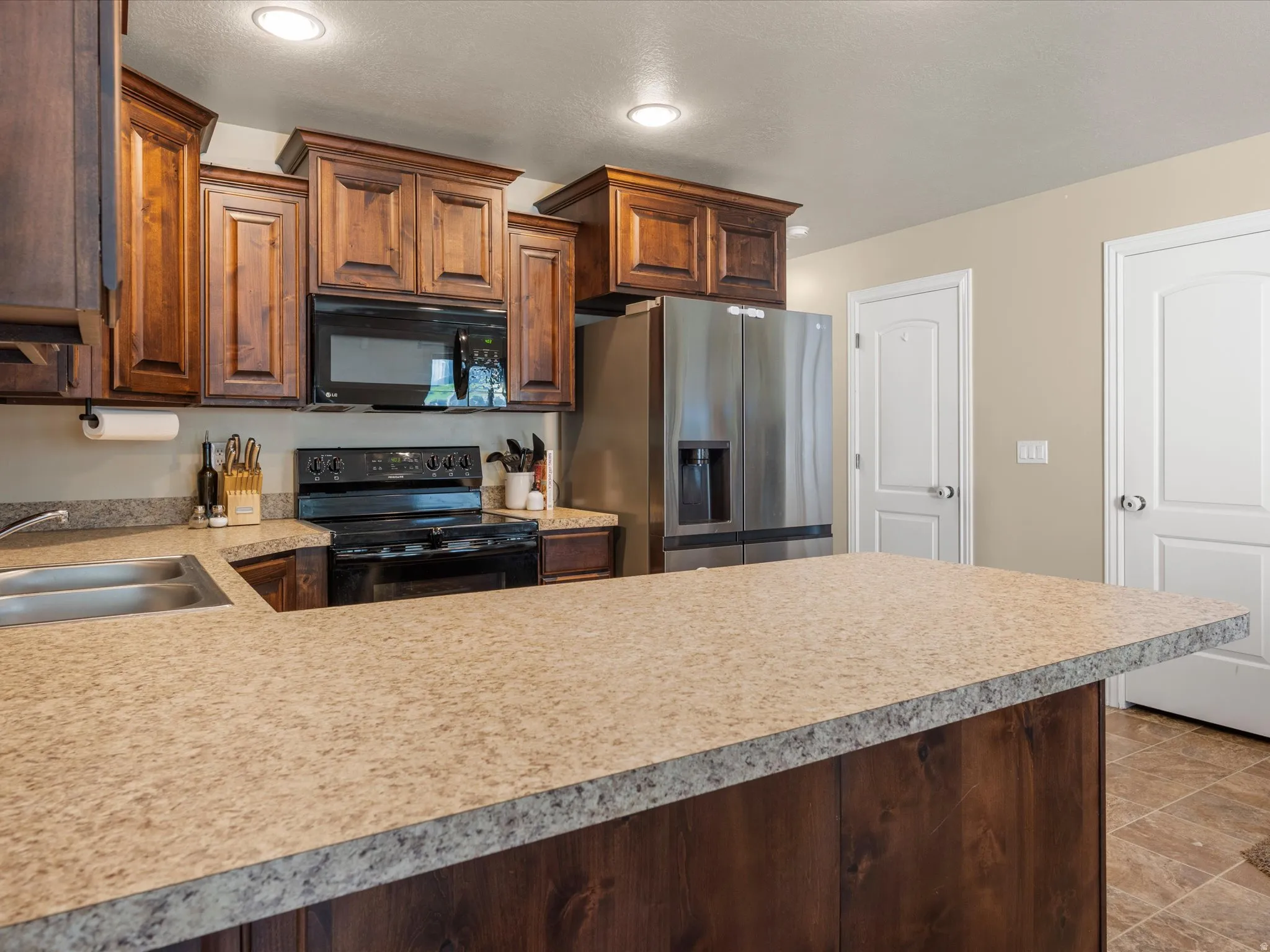 Spacious kitchen featuring dark wood cabinetry, a two-basin stainless steel sink, black electric range with overhead microwave, and ample countertop space