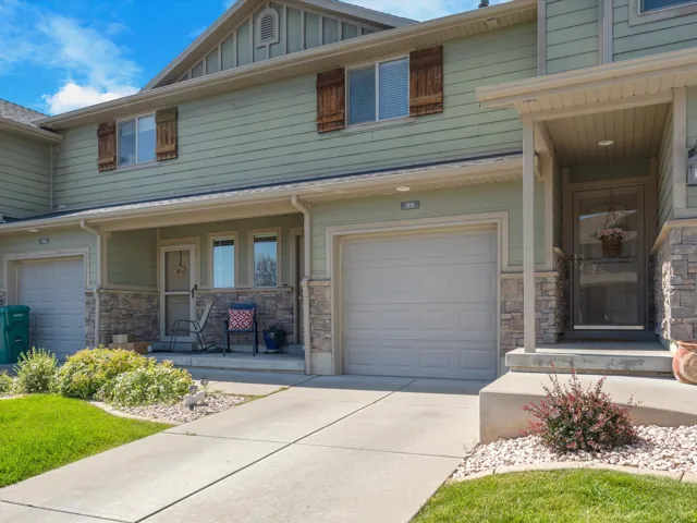 Townhome exterior featuring light green siding, stone veneer accents, an attached garage, and a covered front porch