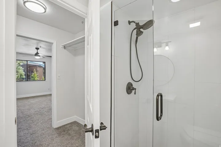 Shower enclosure featuring a frameless glass door, dark bronze fixtures, and white tile surround