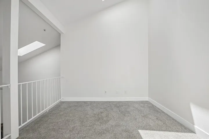 Carpeted loft area featuring a white railing, vaulted ceiling, and a skylight