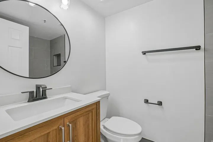 Bathroom featuring a wood-finish vanity with a white countertop and integrated sink, matte black faucet, and a round black-framed mirror